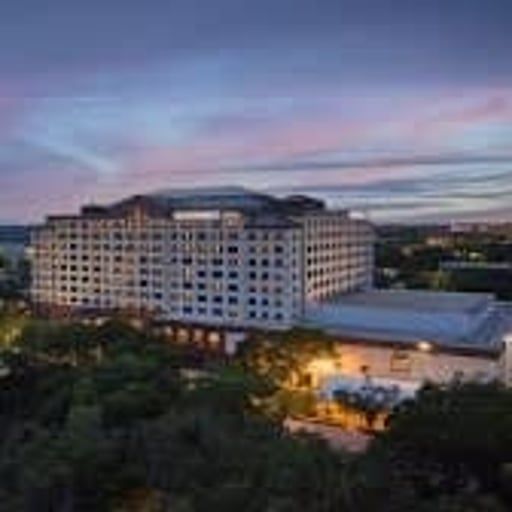 A large, multi-story hotel building surrounded by trees at dusk with a purple and orange sky.