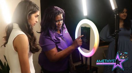 An attendant in a purple shirt guides a person using a ring light photo booth.