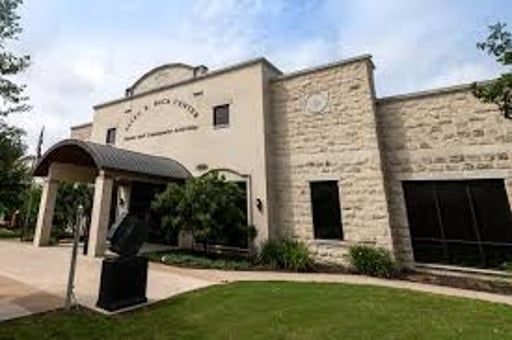The Allen R. Baca Center in Round Rock, Texas, a tan building with stone accents, a dark roof canopy, and landscaping.