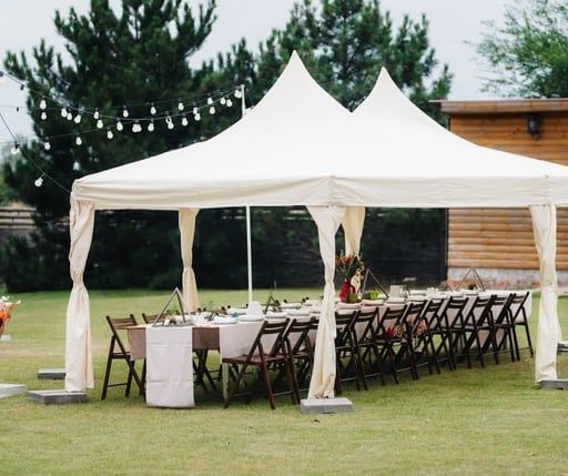 A white event tent on a grassy lawn set up with long banquet tables and chairs for an outdoor gathering.