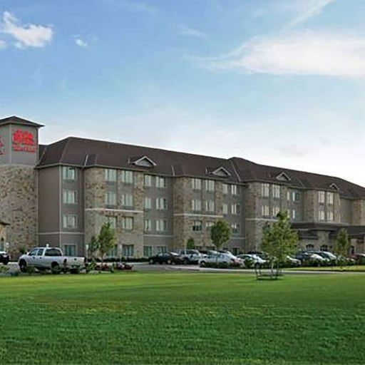 A multi-story tan stone and brown building with a large green lawn in the foreground under a blue sky.