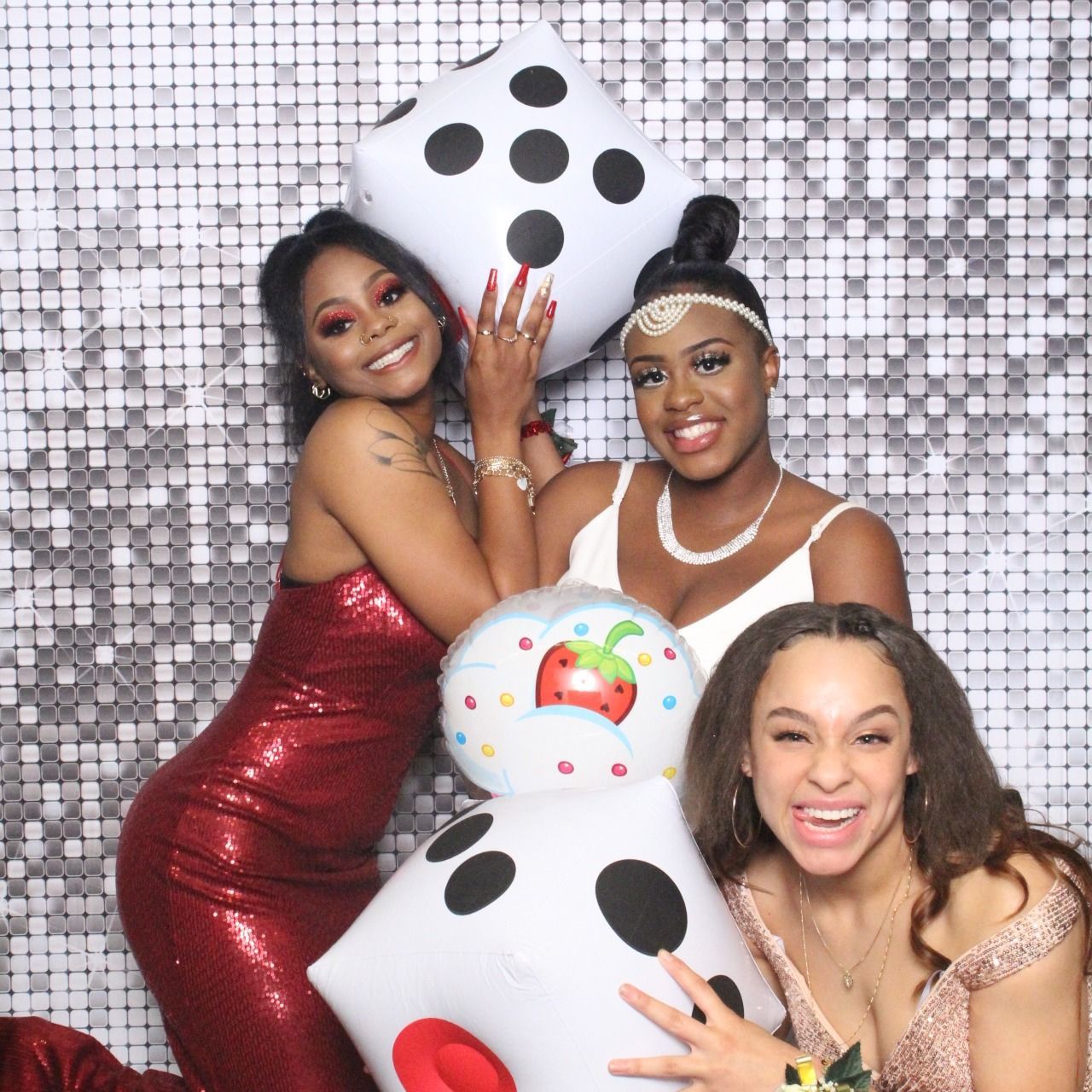Three people pose with oversized dice balloons in front of a silver sequined backdrop.
