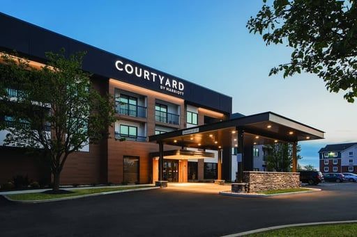 A modern Courtyard by Marriott hotel exterior at twilight with a lit entrance canopy, brick facade, and trees.
