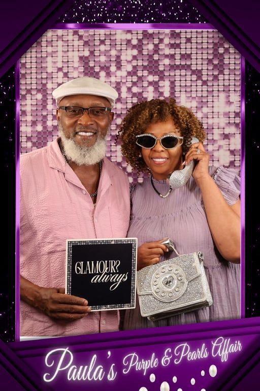 Two people pose in front of a purple backdrop.