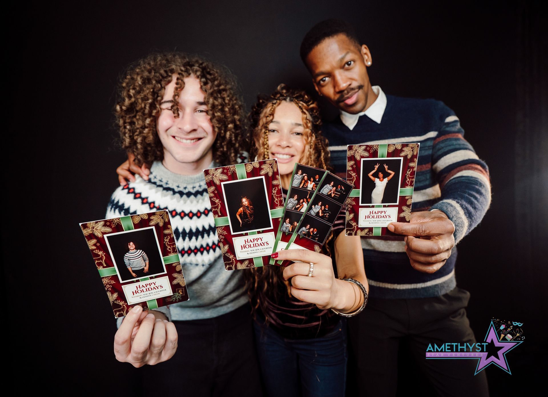 Three people holding holiday cards and smiling against a dark backdrop