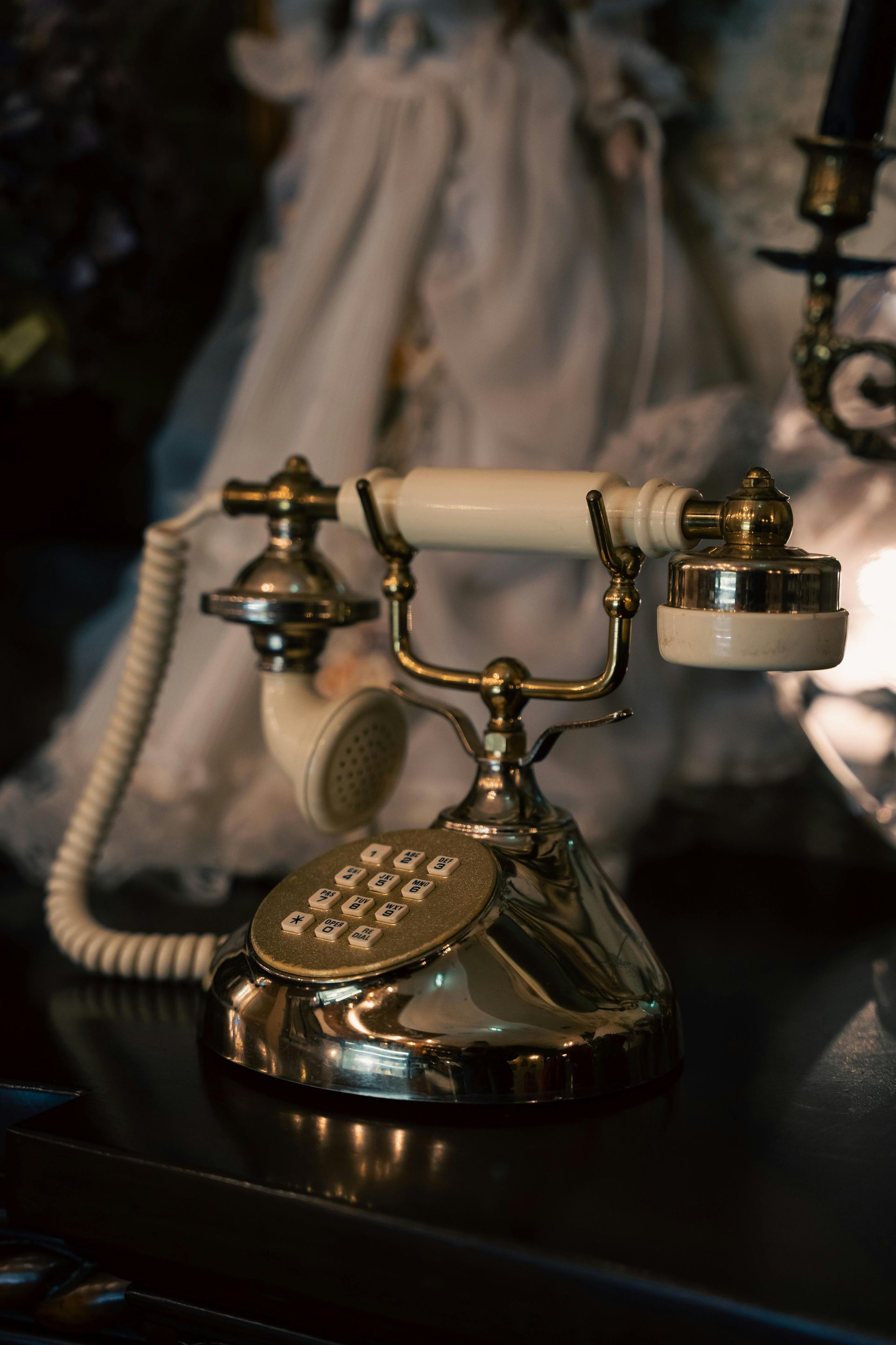 An ornate, vintage-style brass and white telephone rests on a dark surface in front of a blurry, ethereal background.