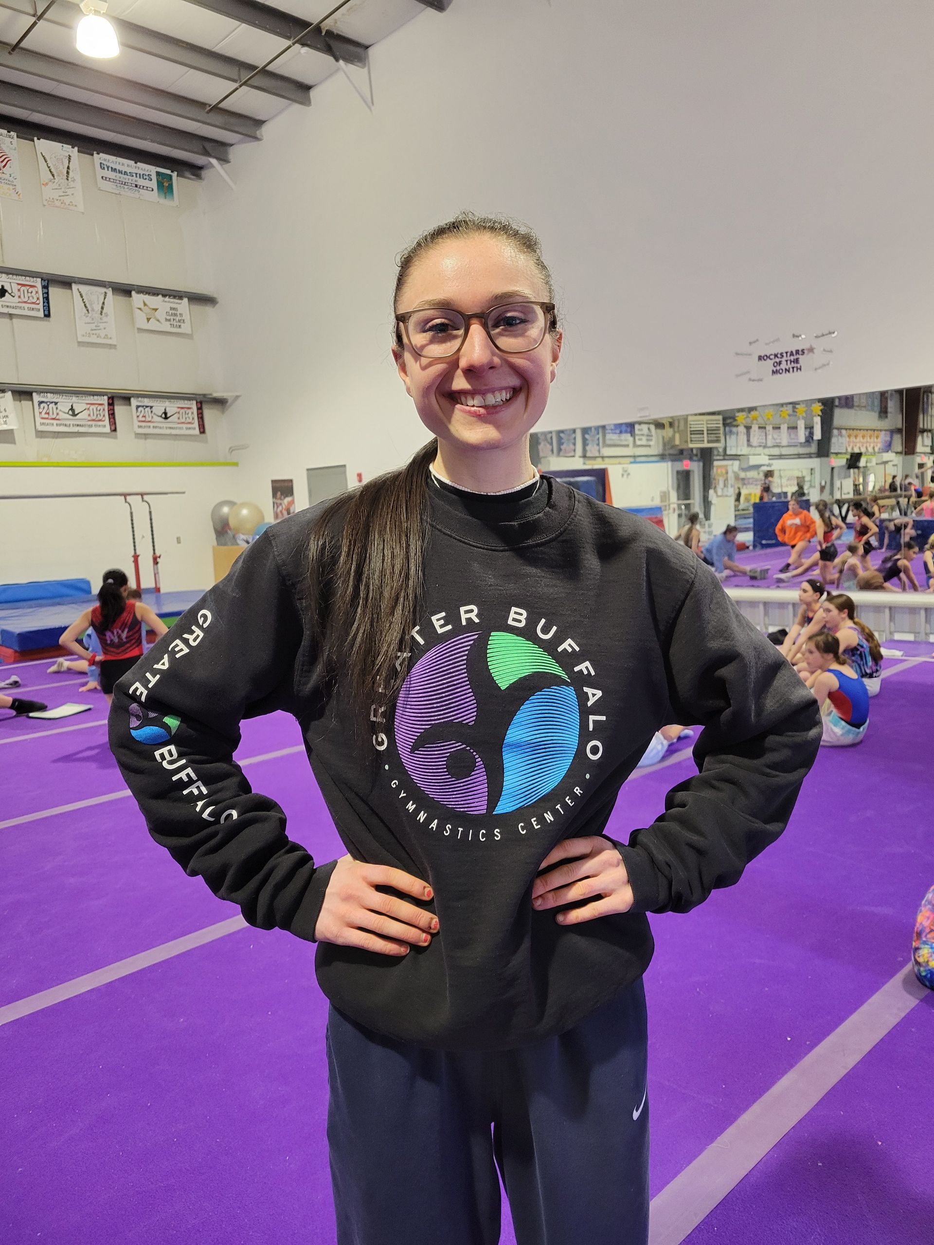 A woman is standing in front of a purple wall in a gym.