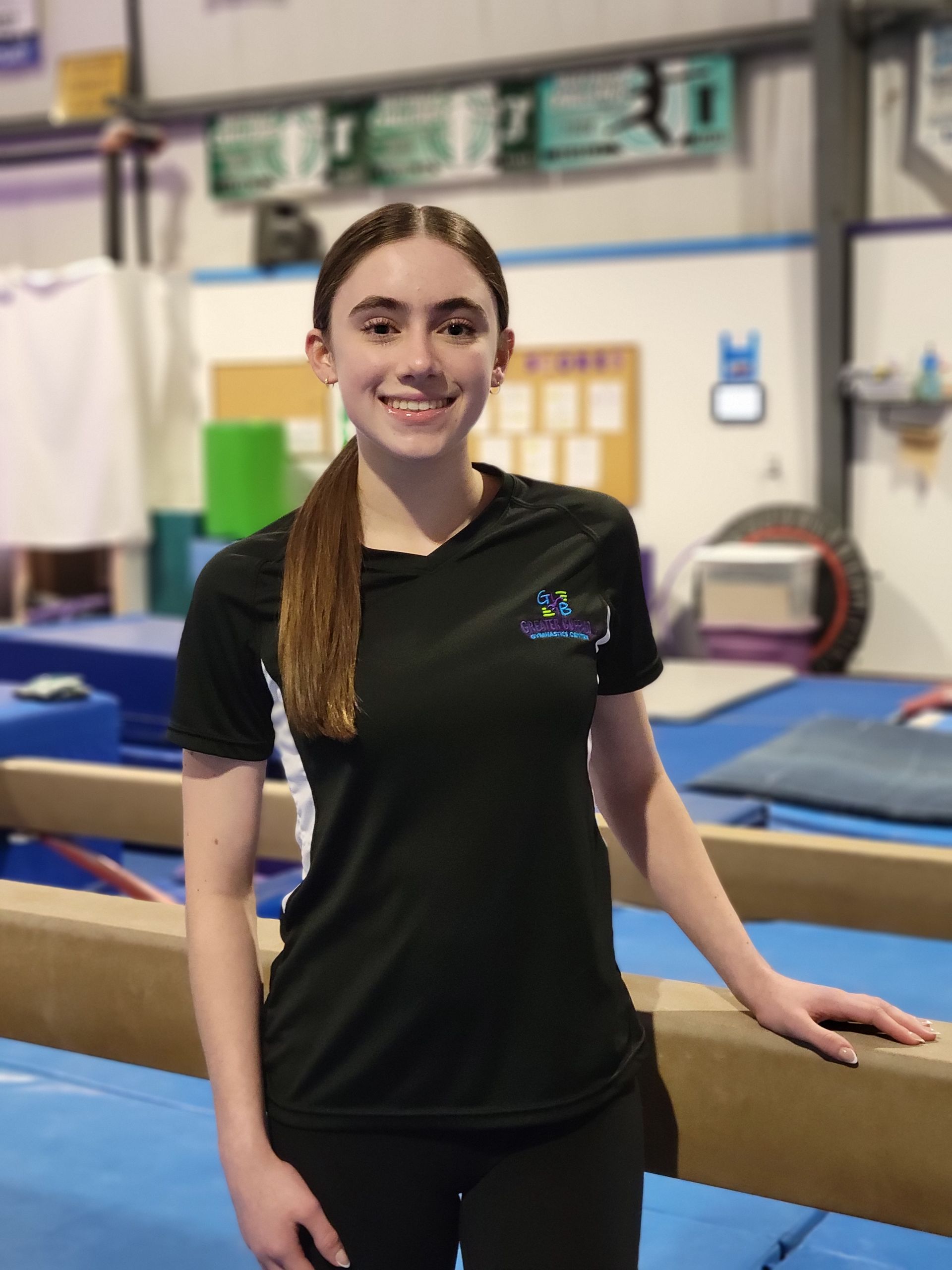 A young girl in a black shirt and shorts is standing in front of a wooden wall.