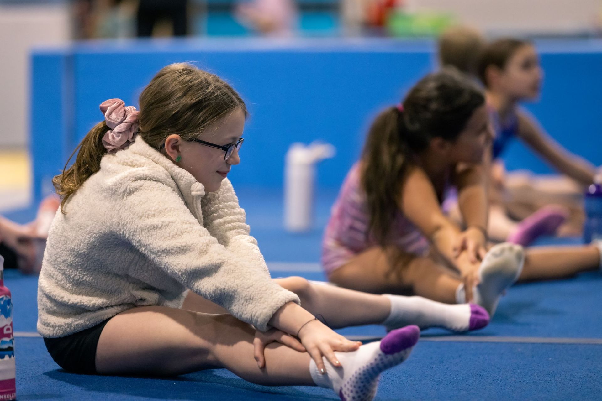 A group of young girls are sitting on the floor stretching their legs.