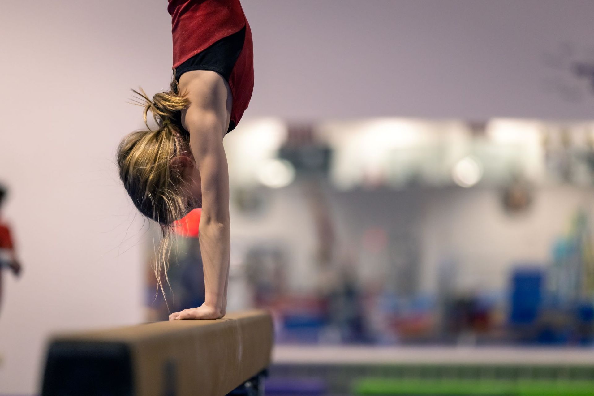 A young girl is doing a handstand on a balance beam.