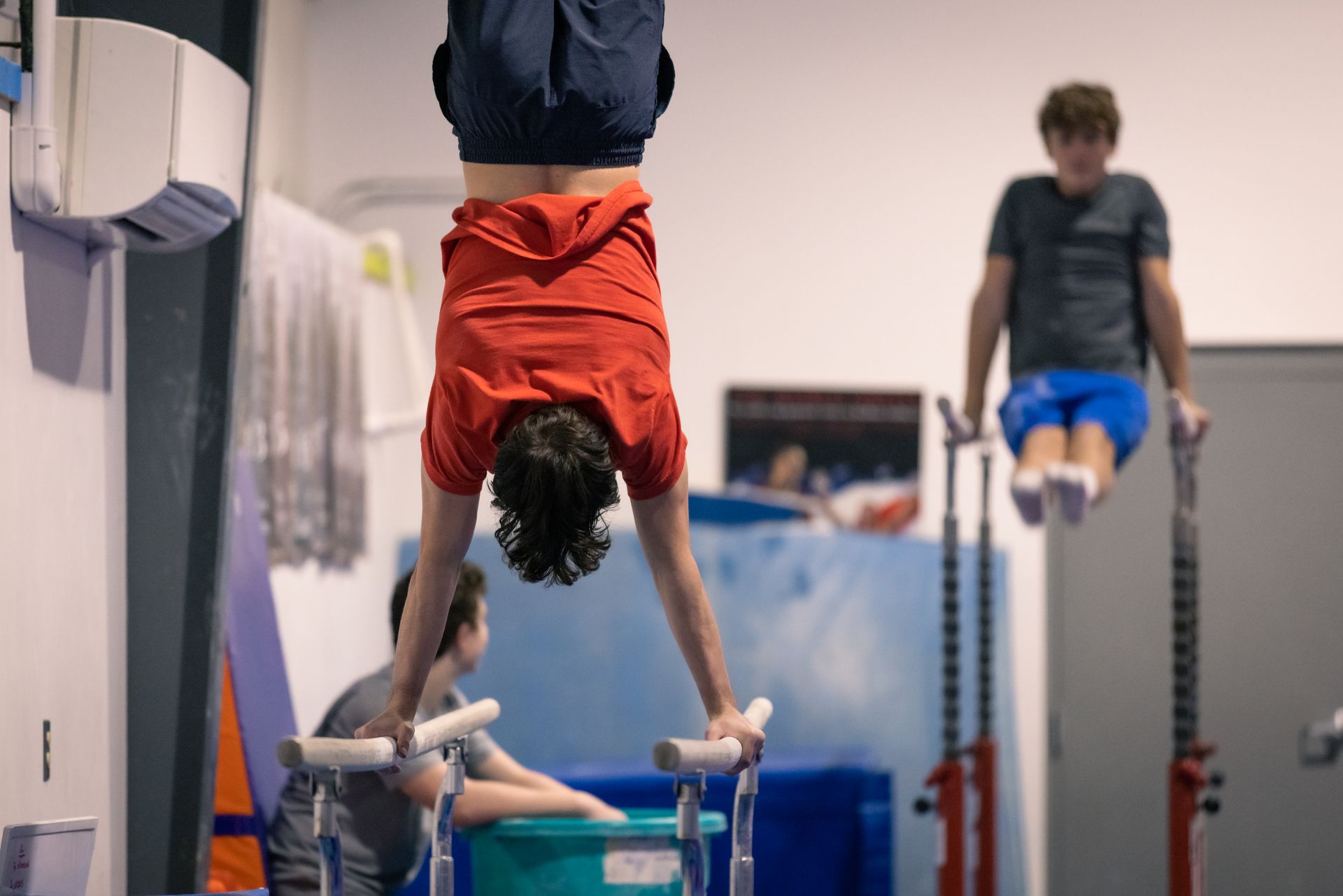 A man is doing a handstand on a parallel bars in a gym.