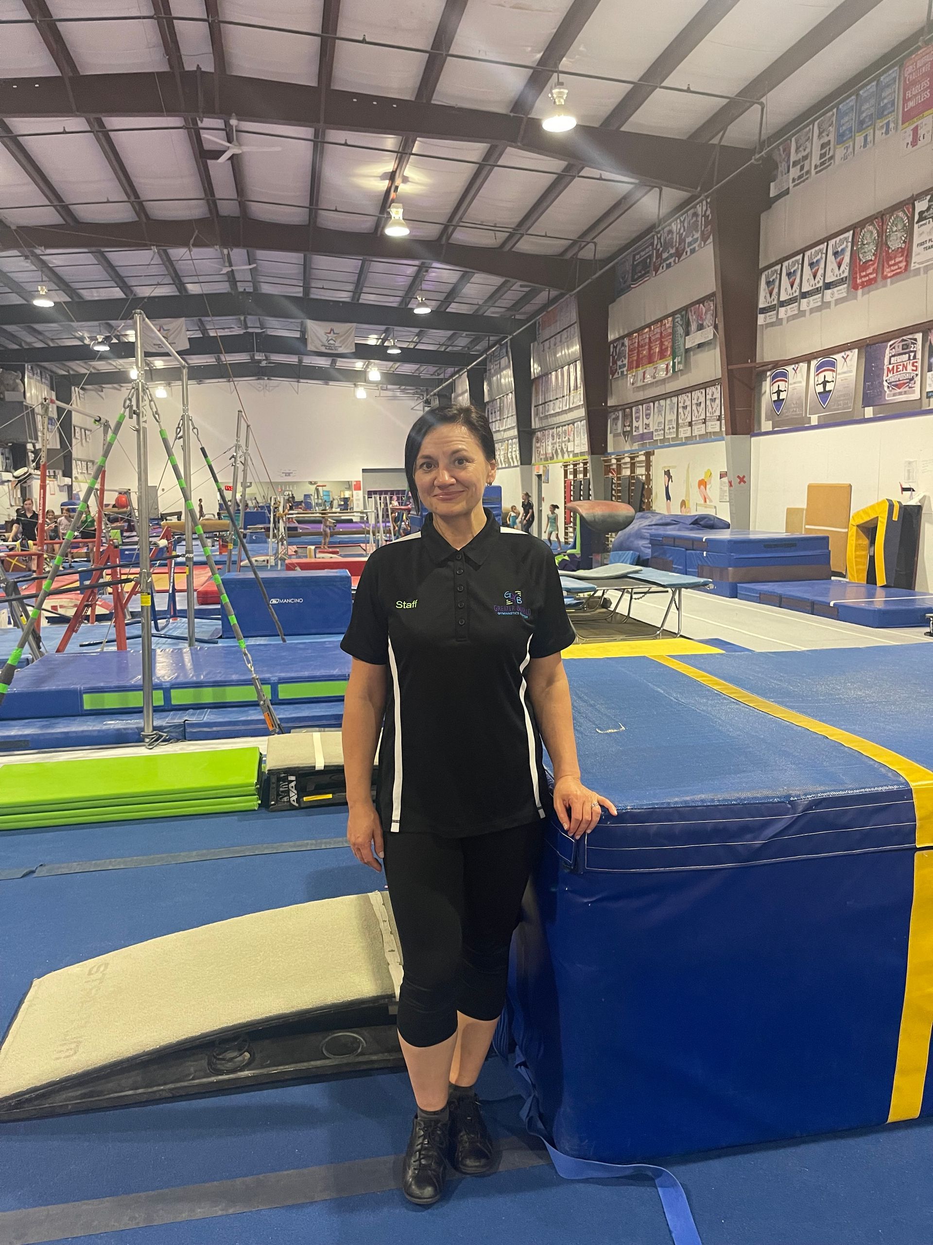 A woman is standing in a gym next to a trampoline.