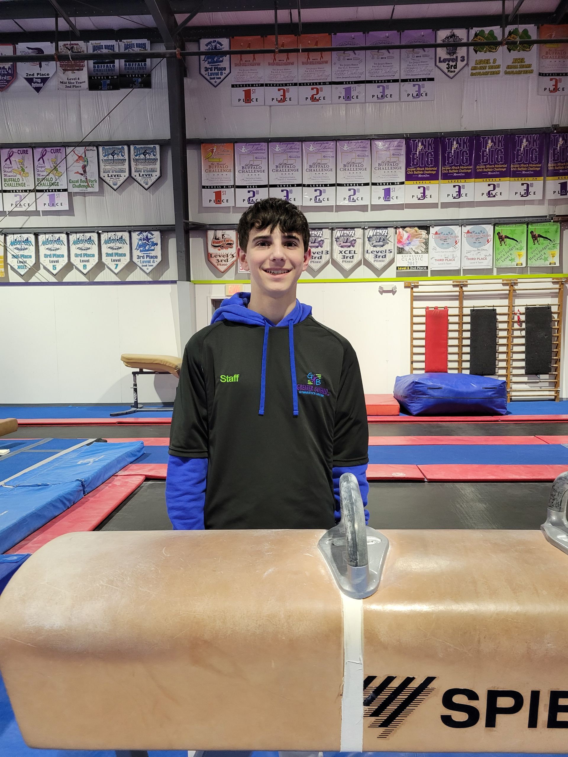 A young man is standing next to a balance beam in a gym.