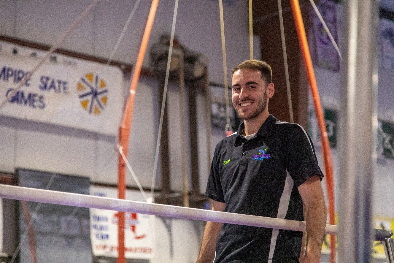 A man is standing on a balance beam in a gym.