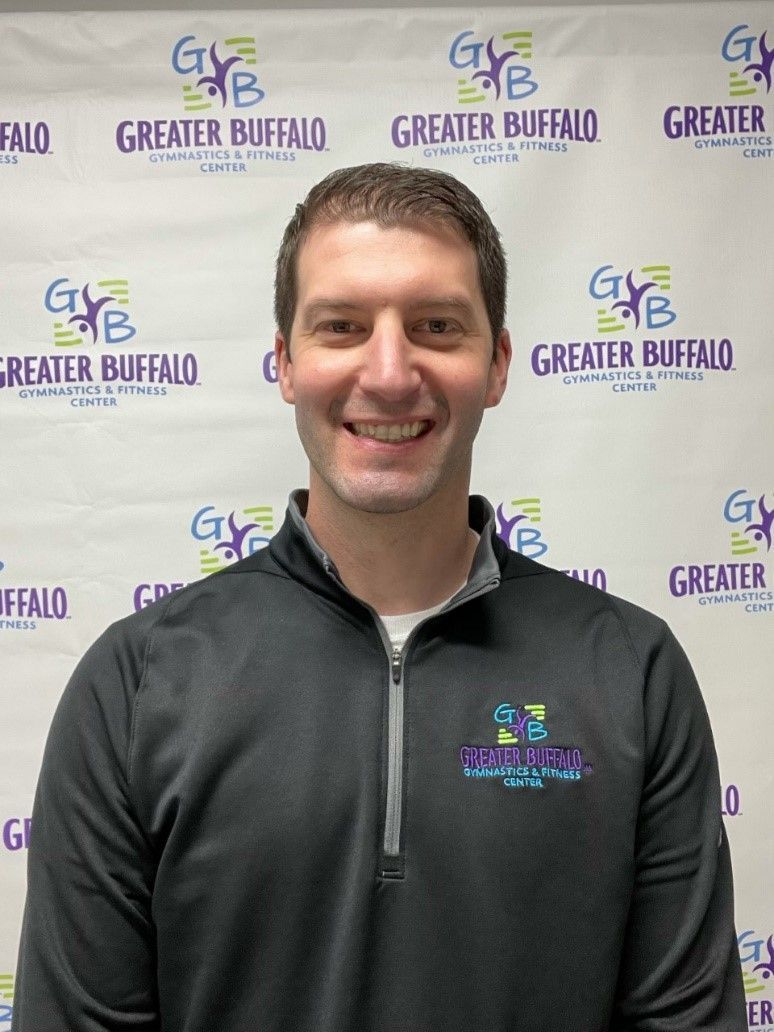 A man is smiling in front of a greater buffalo banner.
