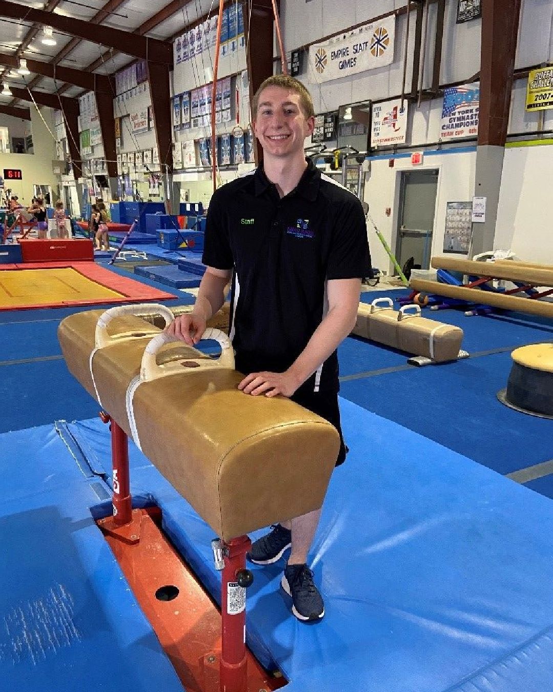 A young man is standing next to a balance beam in a gym.