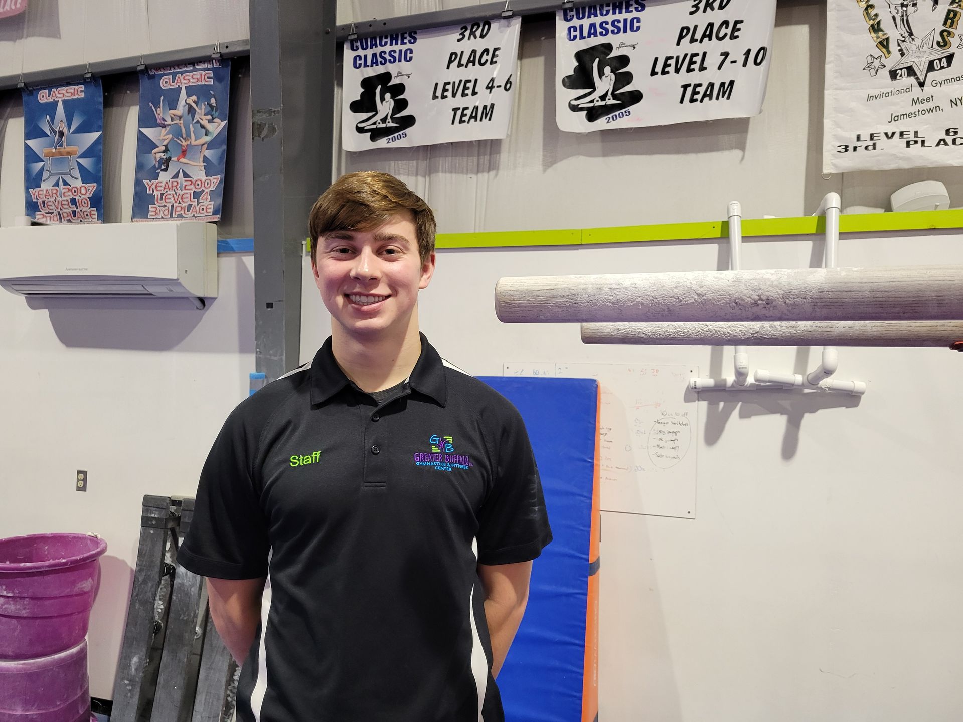 A young boy in a black shirt is standing next to a bar in a gym.