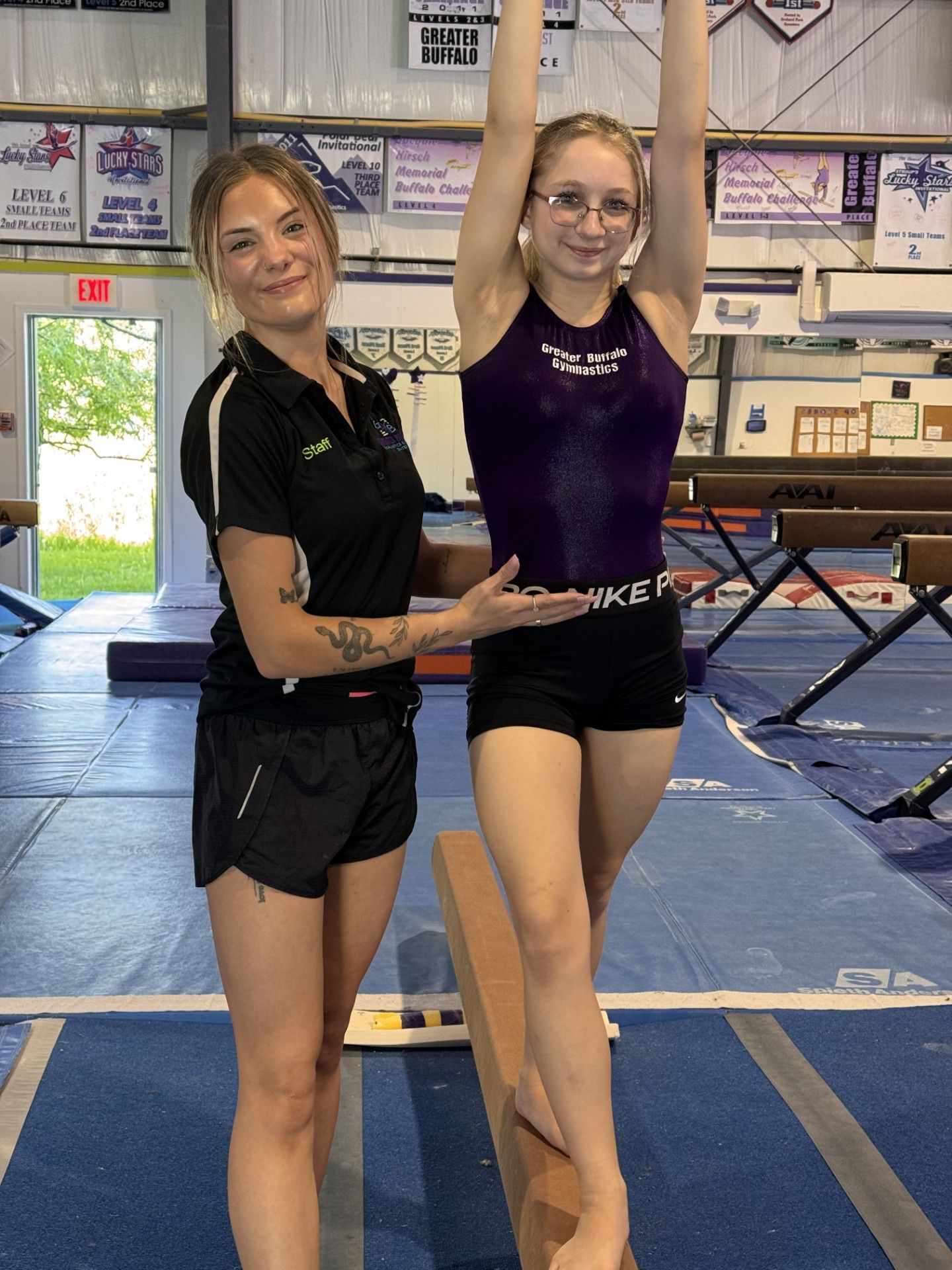 A woman is helping a young girl balance on a balance beam in a gym.