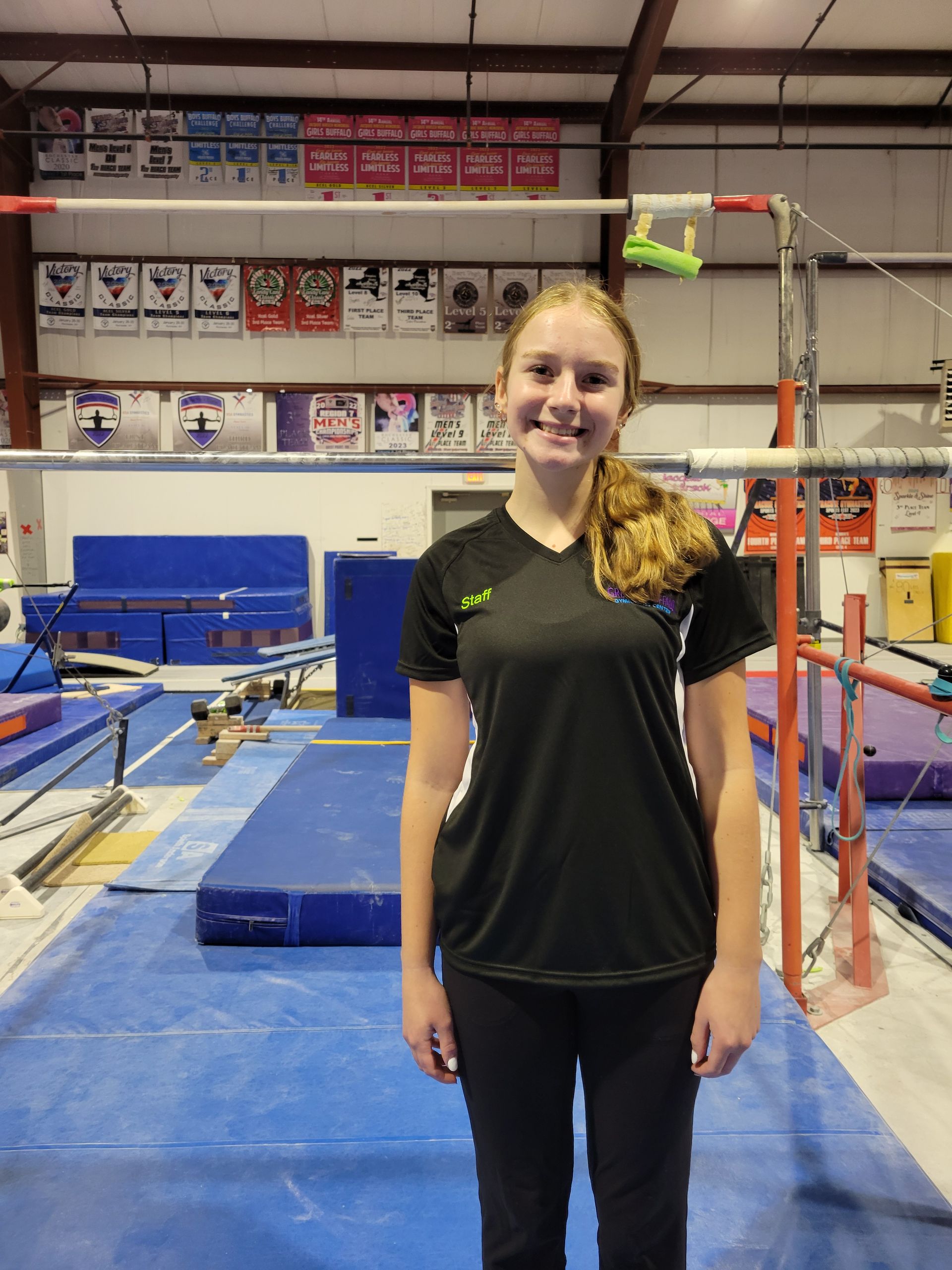 A young girl is standing in front of a gymnastics bar in a gym.