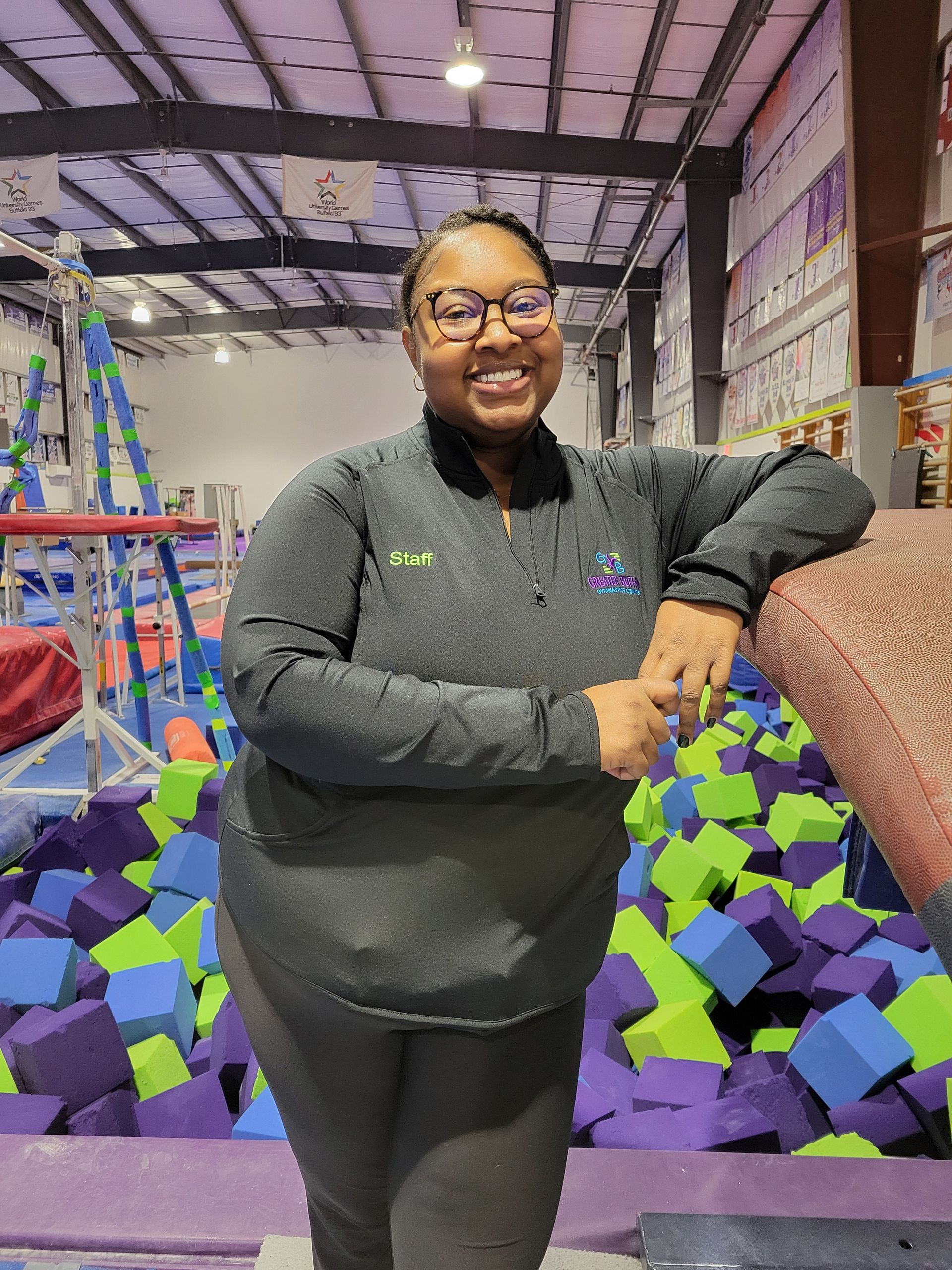 A woman is standing in front of a pile of foam cubes in a gym.