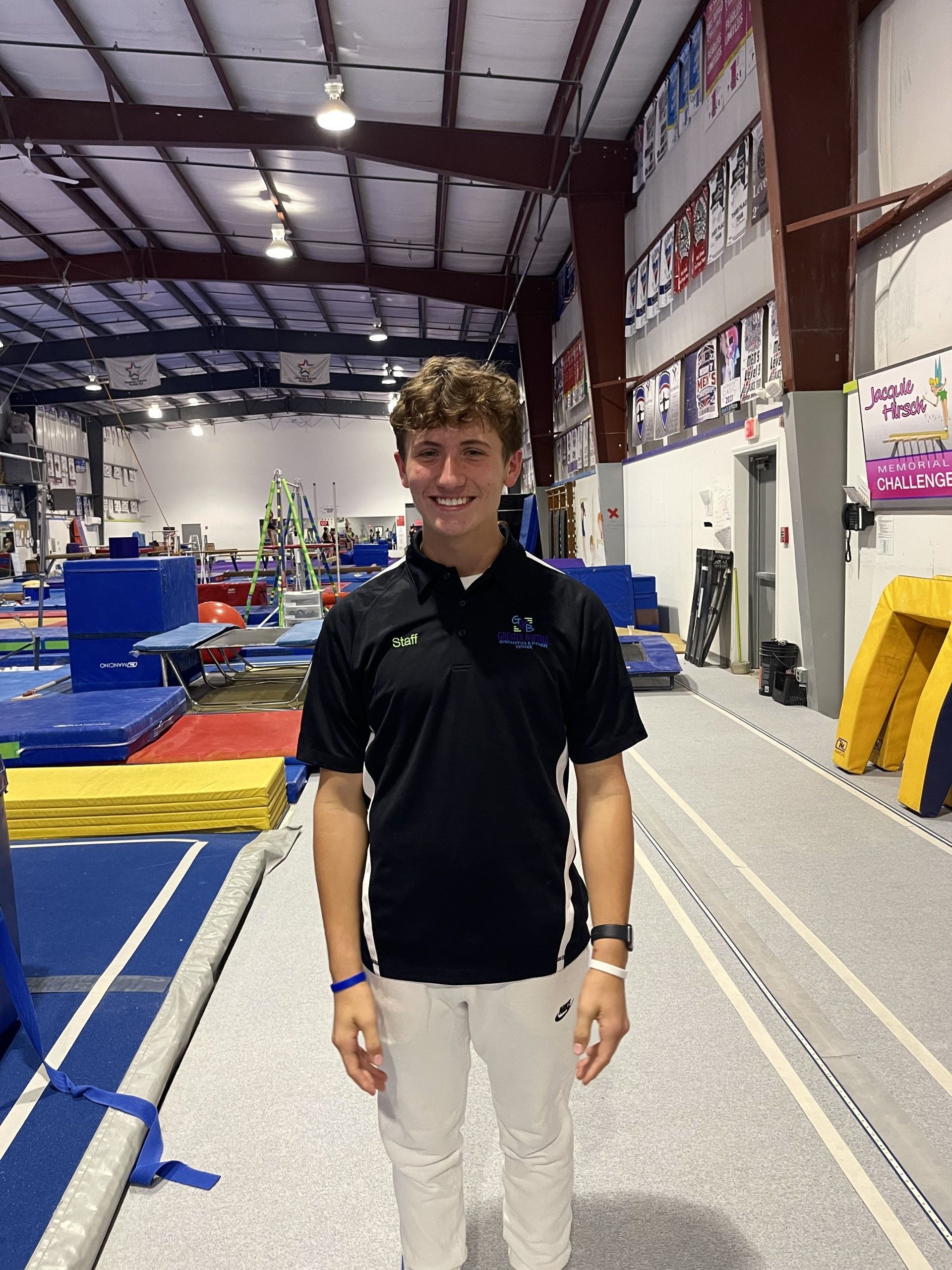 A young man in a black shirt and white pants is standing in a gym.