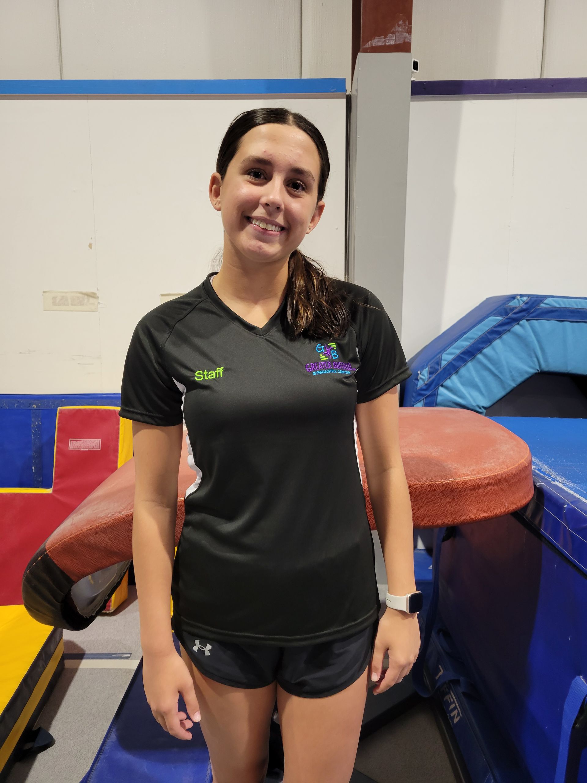 A young woman in a black shirt and shorts is standing in front of a trampoline.