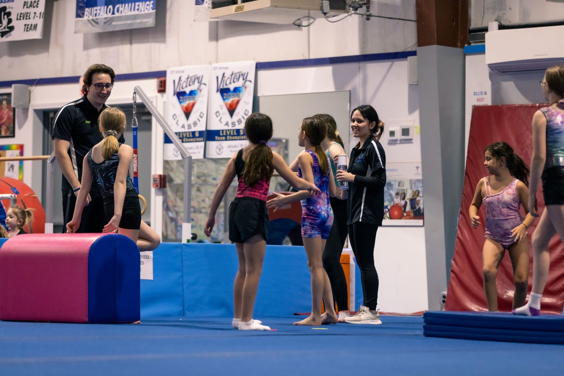 A group of young girls are standing in a gym talking to each other.