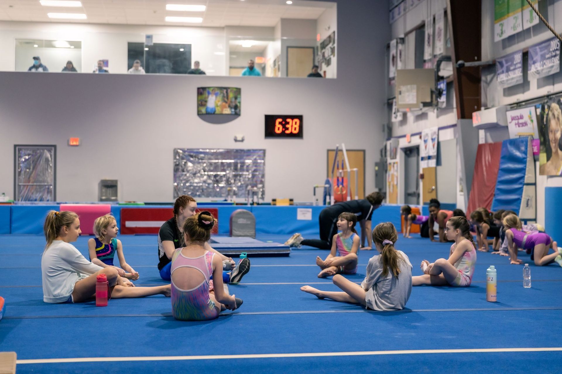 A group of young girls are sitting on the floor of a gym.