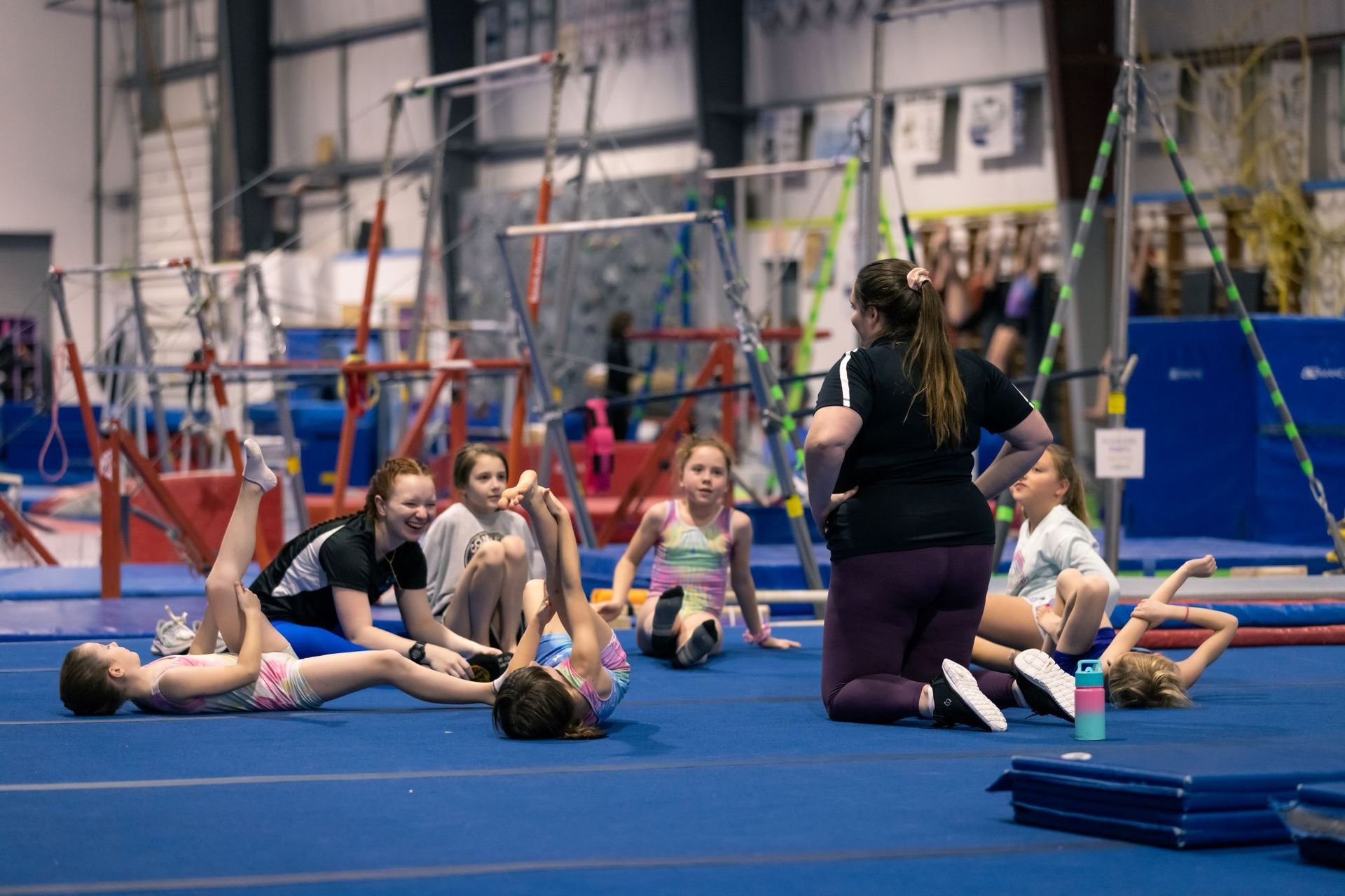 A group of young girls are doing exercises on the floor in a gym.