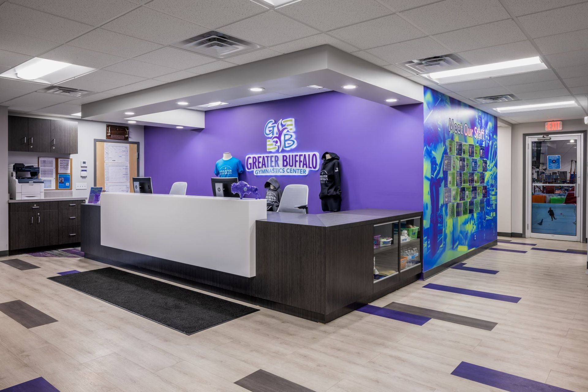 A reception area in a gym with purple walls and a white counter.