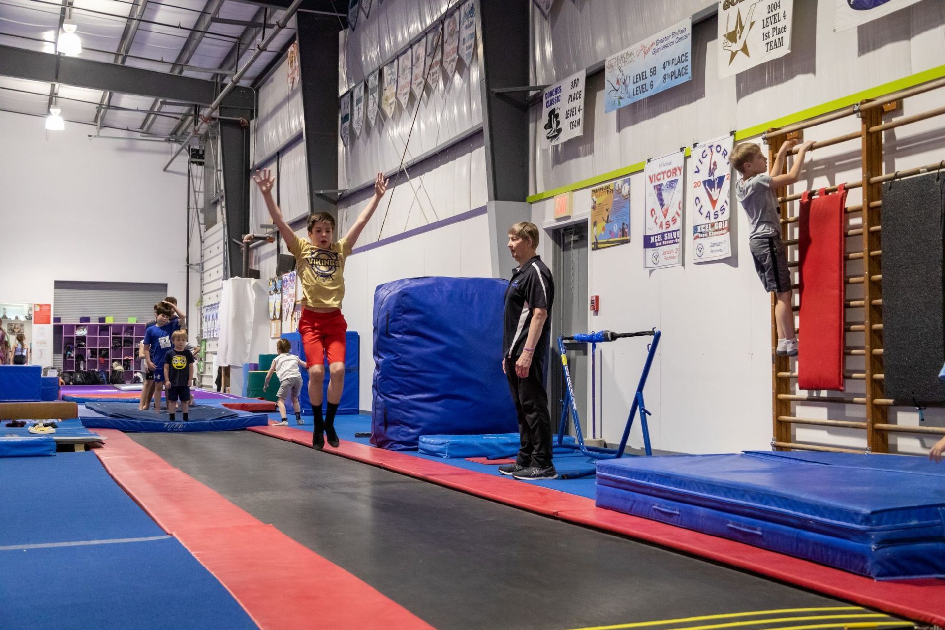 A boy is jumping on a trampoline in a gym.