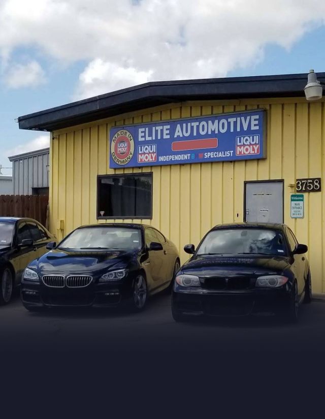 An automotive shop with five cars parked outside. Yellow building with a sign that reads, 