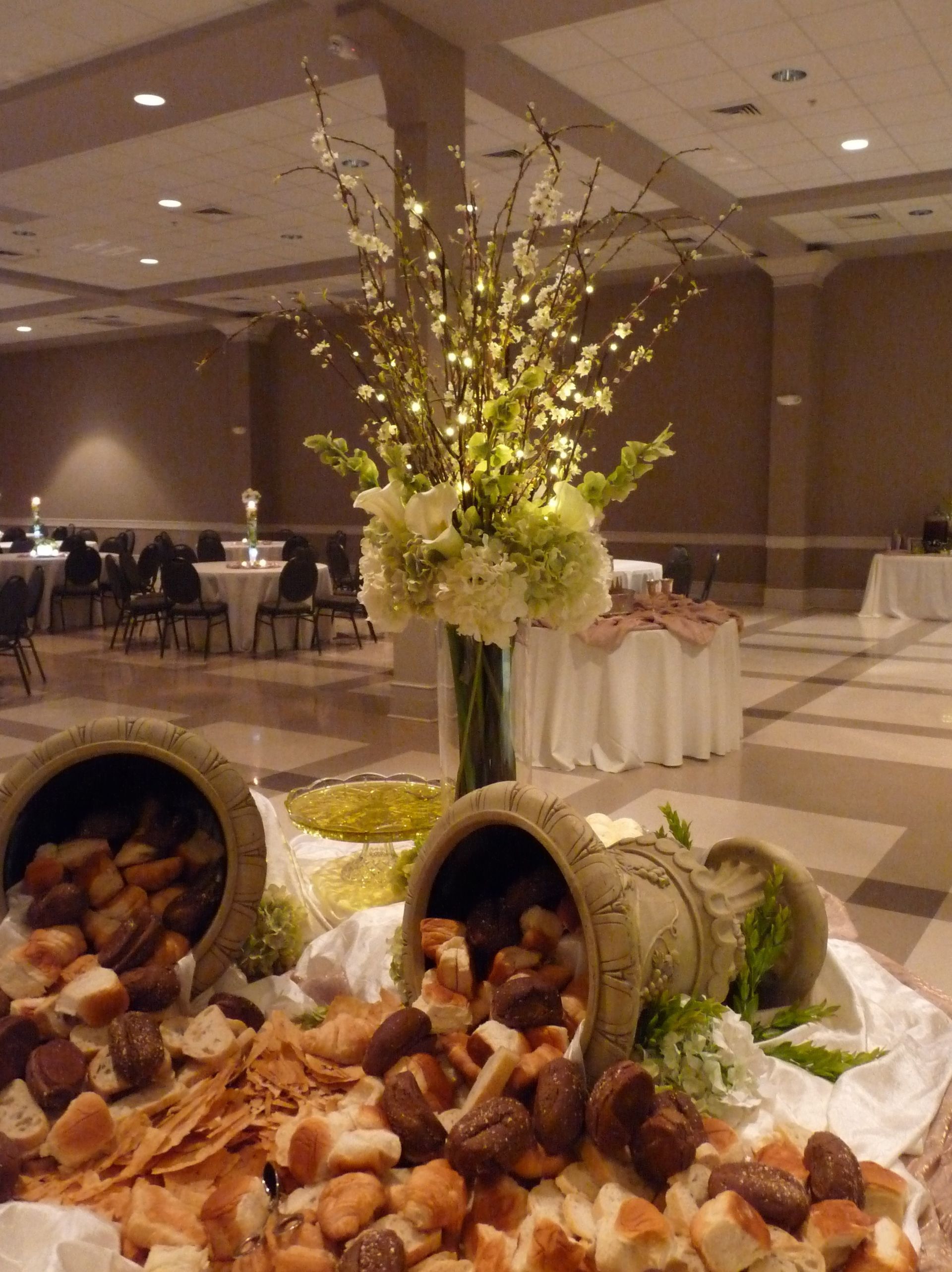 Elegant banquet hall display with tipped barrels spilling bread rolls beside a tall floral centerpiece.