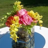Colorful pink and yellow flower bouquet in a glass vase on a white table outdoors