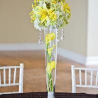 Tall clear vase with yellow and white flowers on a table at a formal event