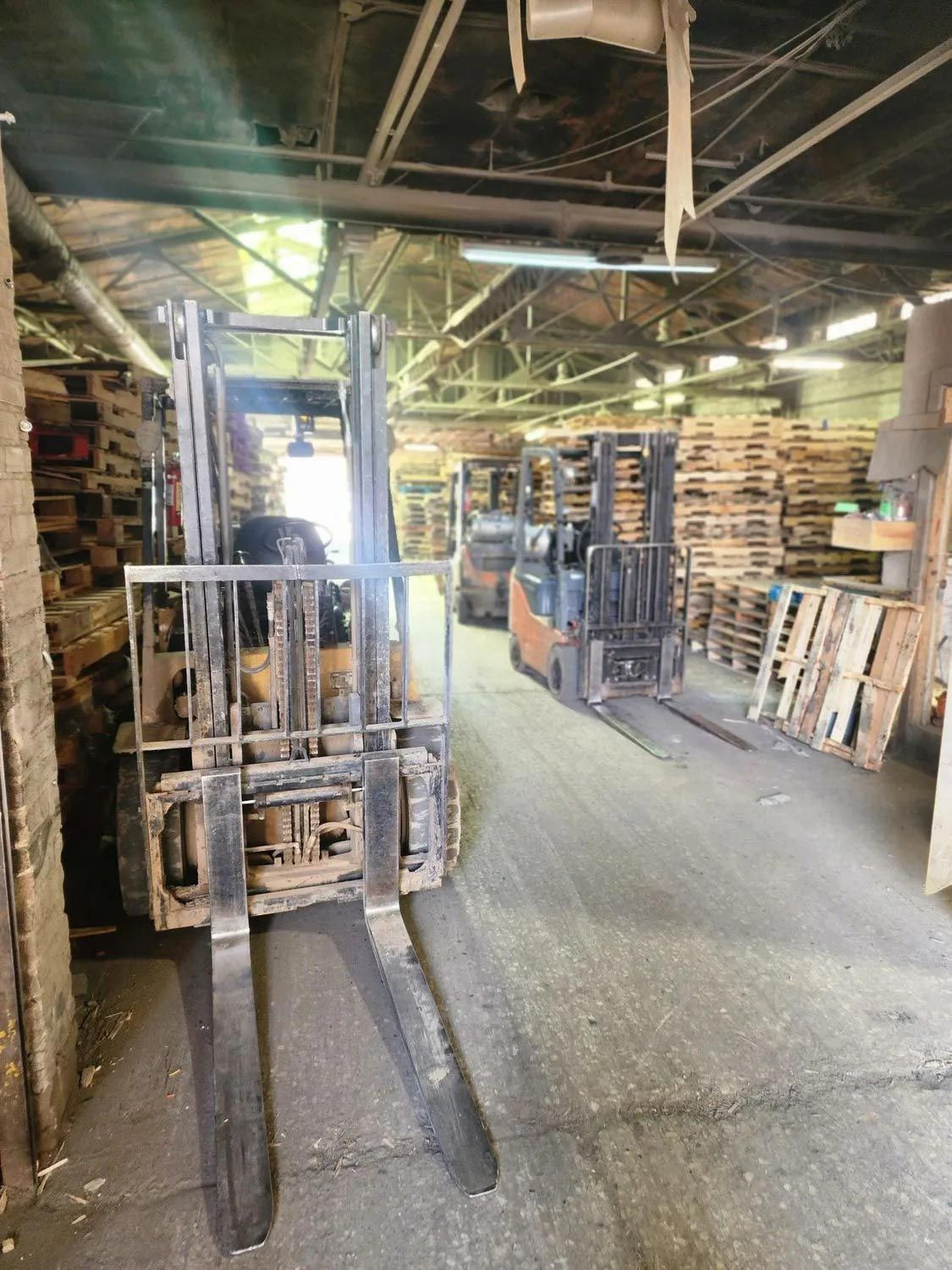 A forklift is driving through a warehouse filled with wooden pallets.