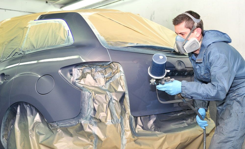 A Man Wearing A Mask Is Painting A Car In A Garage — K & D Auto Repair in Cardiff, NSW