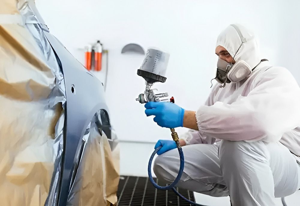 A Man Is Spray Painting A Car In A Garage — K & D Auto Repair in Cardiff, NSW