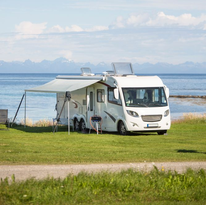 White RV Parked on Grass Near the Ocean, Awning Extended on a Sunny Day — Darren's Caravan Repairs in Lake Macquarie, NSW