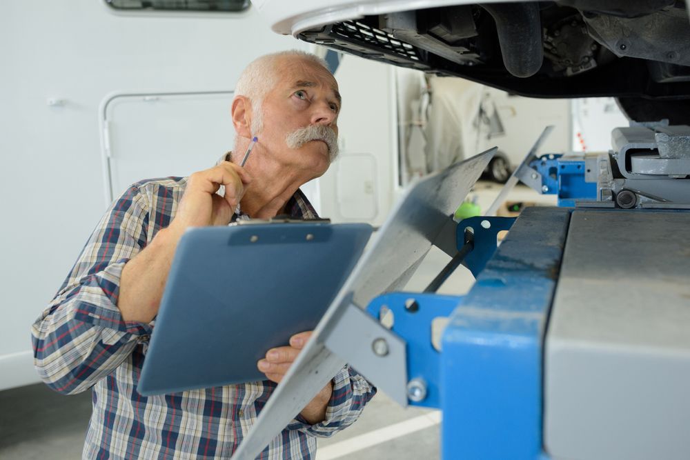 Senior Man Inspecting Vehicle Undercarriage With Clipboard in Auto Repair Shop — Darren's Caravan Repairs in Central Coast, NSW