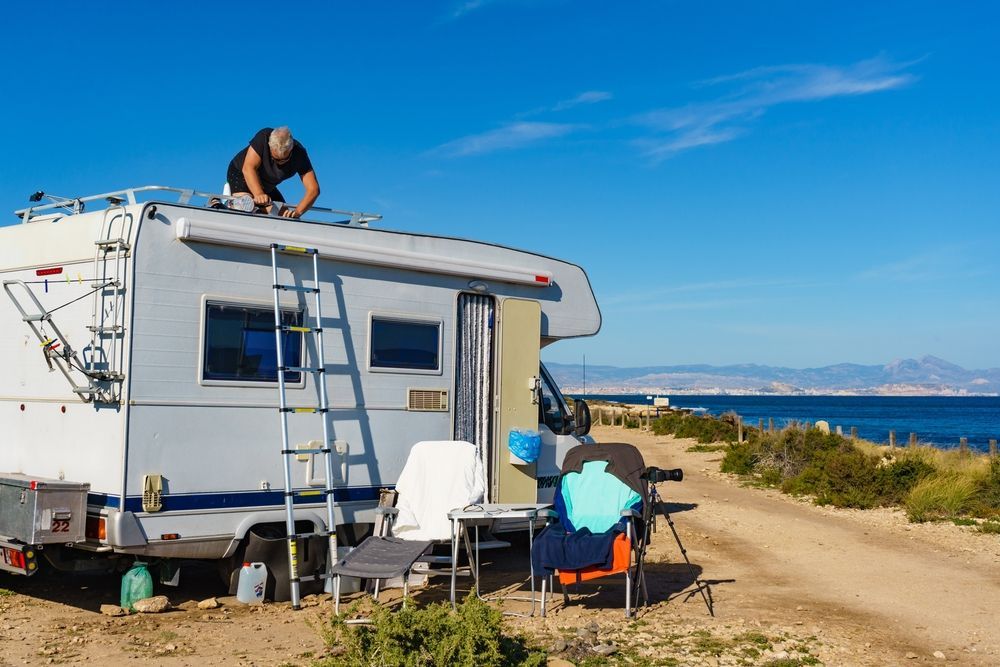 Man on RV roof, Working on White RV, Blue Sky, Table and Chairs Outside — Darren's Caravan Repairs in Warners Bay, NSW