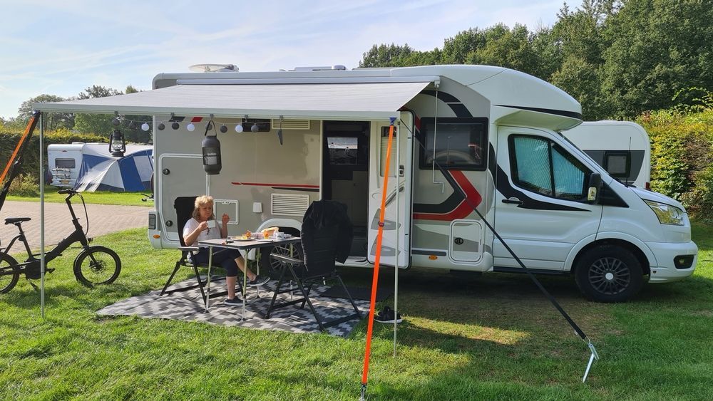 Person Eating at a Table Outside a White RV With Awning Extended on a Grassy Campsite — Darren's Caravan Repairs in Warners Bay, NSW