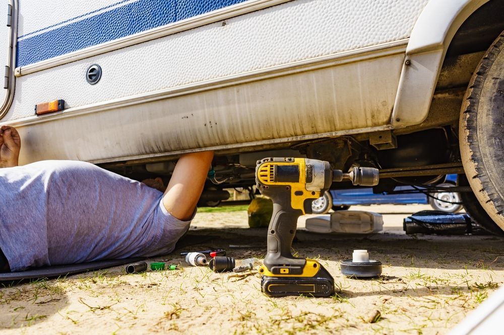 Person Working Under a Motorhome, Using a Yellow and Black Power Drill — Darren's Caravan Repairs in Central Coast, NSW