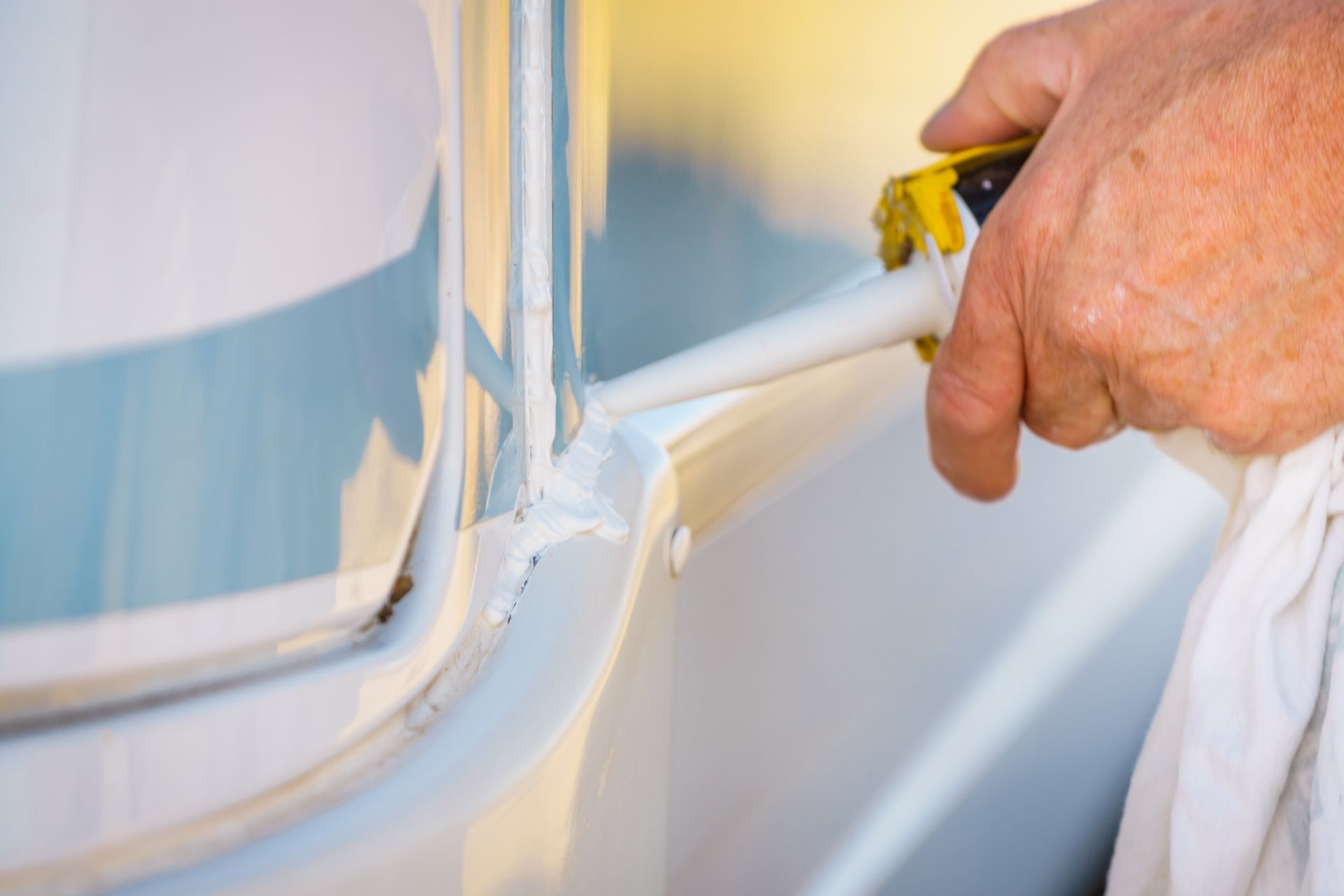 Person Caulking a White Seam on a Vehicle With a White Caulk Gun, Wiping With a White Cloth — Darren's Caravan Repairs in Warners Bay, NSW