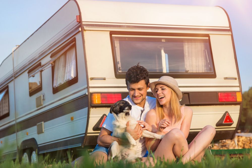 Couple Sitting With Dog in Front of a Camper, Laughing on a Sunny Day — Darren's Caravan Repairs in Warners Bay, NSW