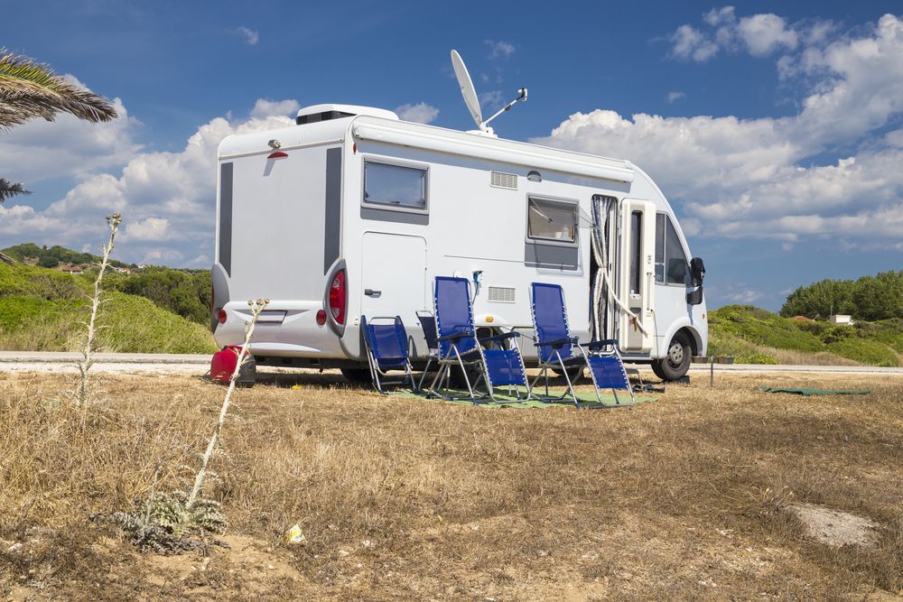 White Rv Parked Outdoors With Blue Chairs and a Satellite Dish, Under a Blue Sky — Darren's Caravan Repairs in Warners Bay, NSW