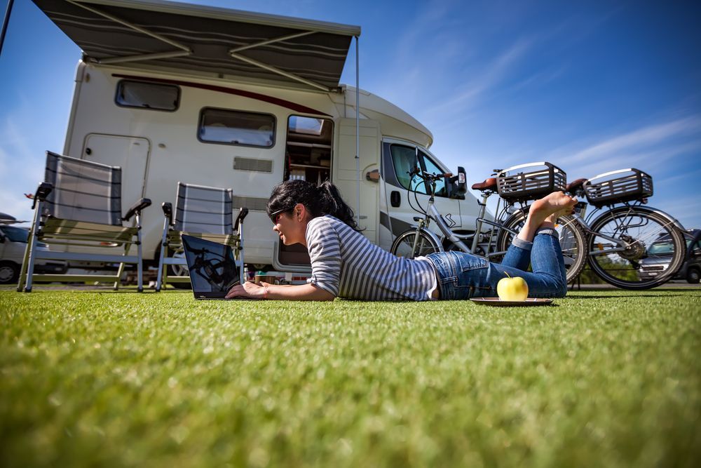 Woman on Grass, Laptop in Front, by a Motorhome — Darren's Caravan Repairs in Lake Macquarie, NSW