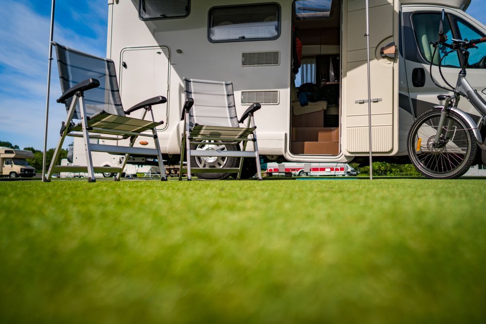 RV Parked on Green Grass With Chairs Set Up Outside, a Bicycle, and Open Door — Darren's Caravan Repairs in Warners Bay, NSW