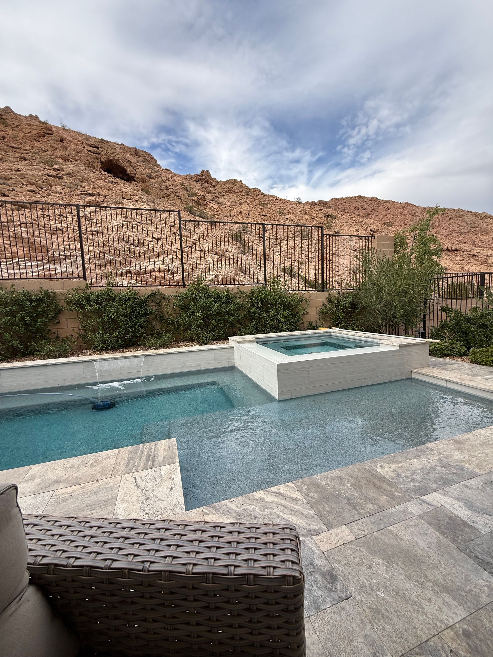 Pool area with a small pool and hot tub, surrounded by stone patio. Rocky mountains in the background.