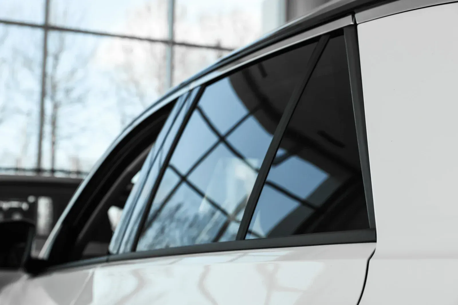 Close-up of car window with tinted glass; white car body visible, with reflection of interior.